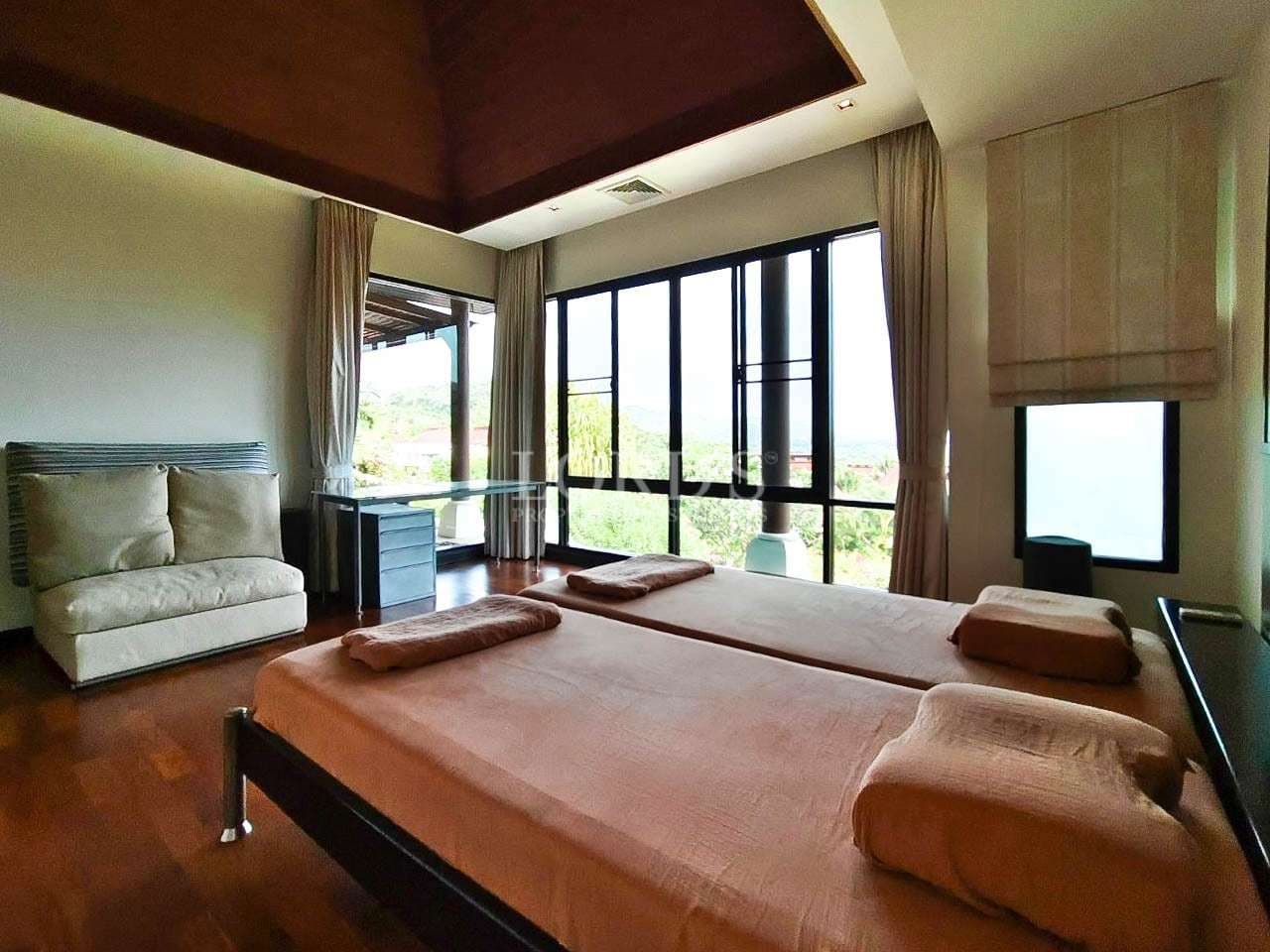 Luxury bedroom with twin beds, wooden flooring, floor-to-ceiling glass windows, and scenic outdoor views.