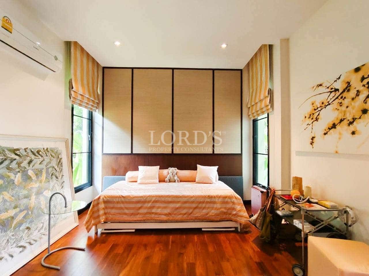 Modern bedroom with wooden flooring, double bed, large windows, and warm neutral interior design.