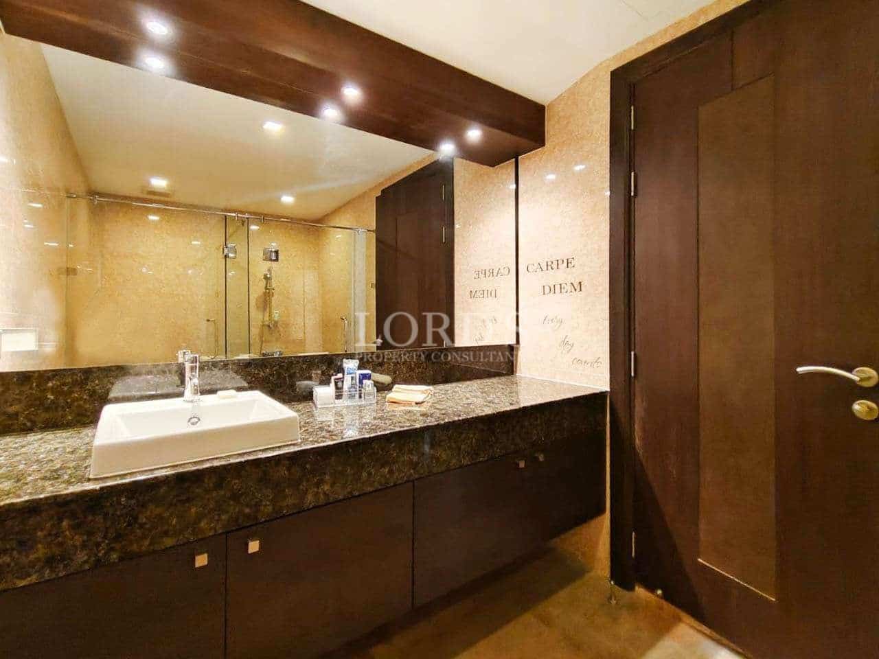 Luxury bathroom with granite vanity countertop, large mirror, glass shower, and warm ambient lighting.