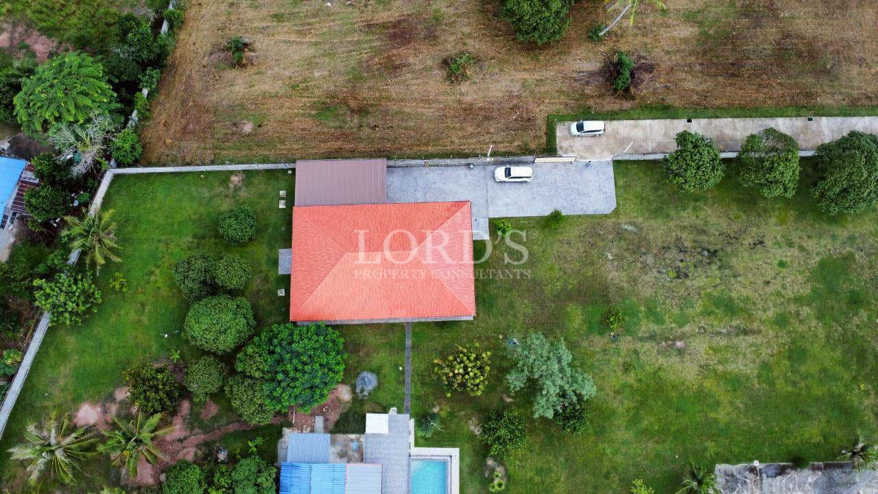 Top-down aerial view of a villa with red roof, private driveway, and large green land plot.