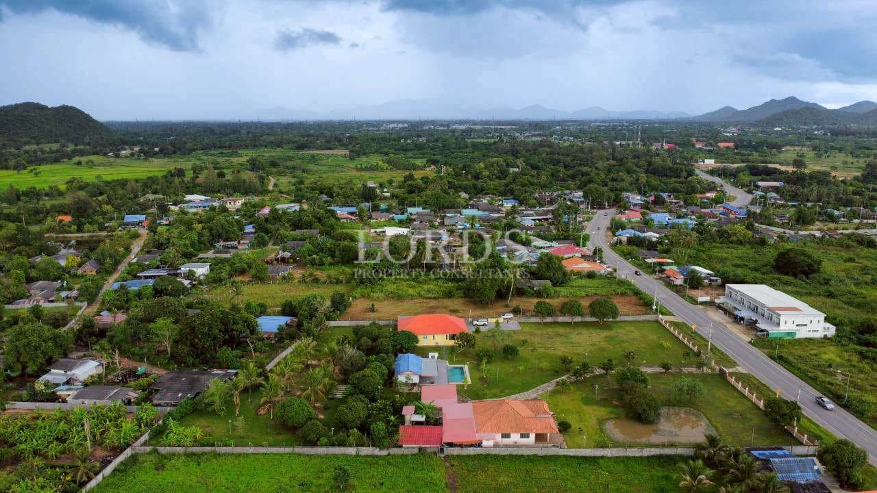 Wide aerial view of residential area with greenery, roads, and surrounding hills.