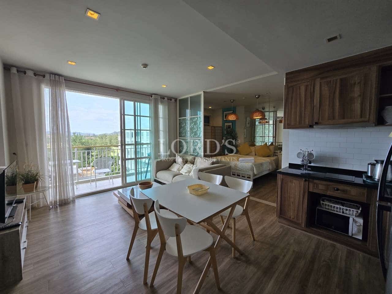 Modern open-plan apartment with dining table, kitchen, living area, and balcony access