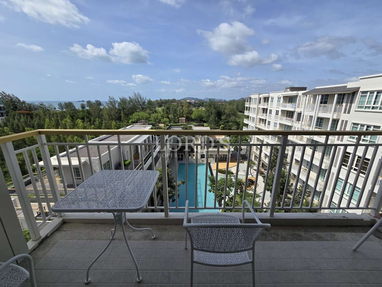 Apartment balcony with outdoor table and chairs overlooking swimming pool and residential buildings