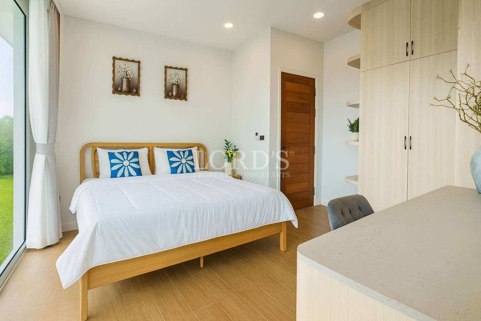 Bright modern bedroom with wooden bed frame, built-in wardrobe, work desk, and large window with natural light