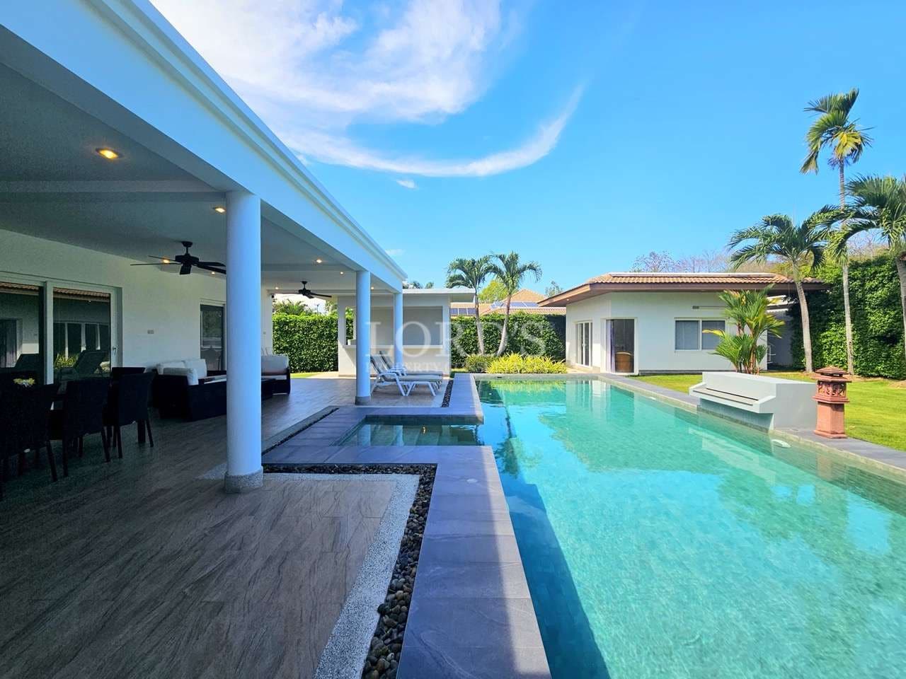 Modern luxury villa with private swimming pool, covered outdoor patio, palm trees, and bright blue tropical sky.