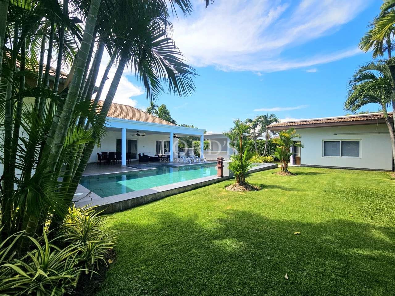 Tropical luxury villa garden with private swimming pool, palm trees, and covered outdoor seating area.