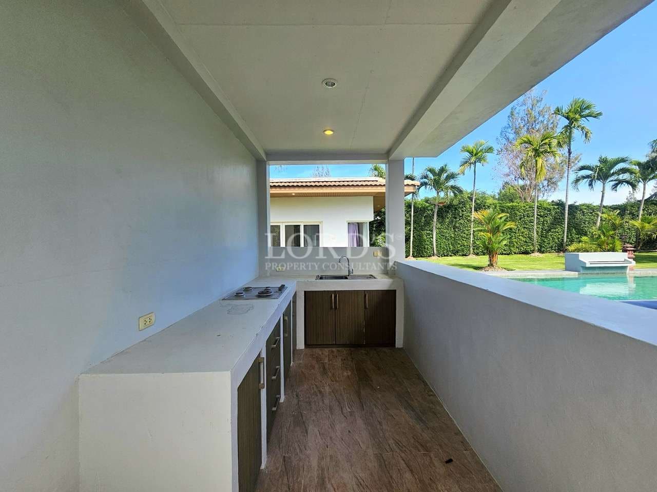 Covered outdoor kitchenette with built-in counter, storage cabinets, and pool view in a luxury tropical villa.
