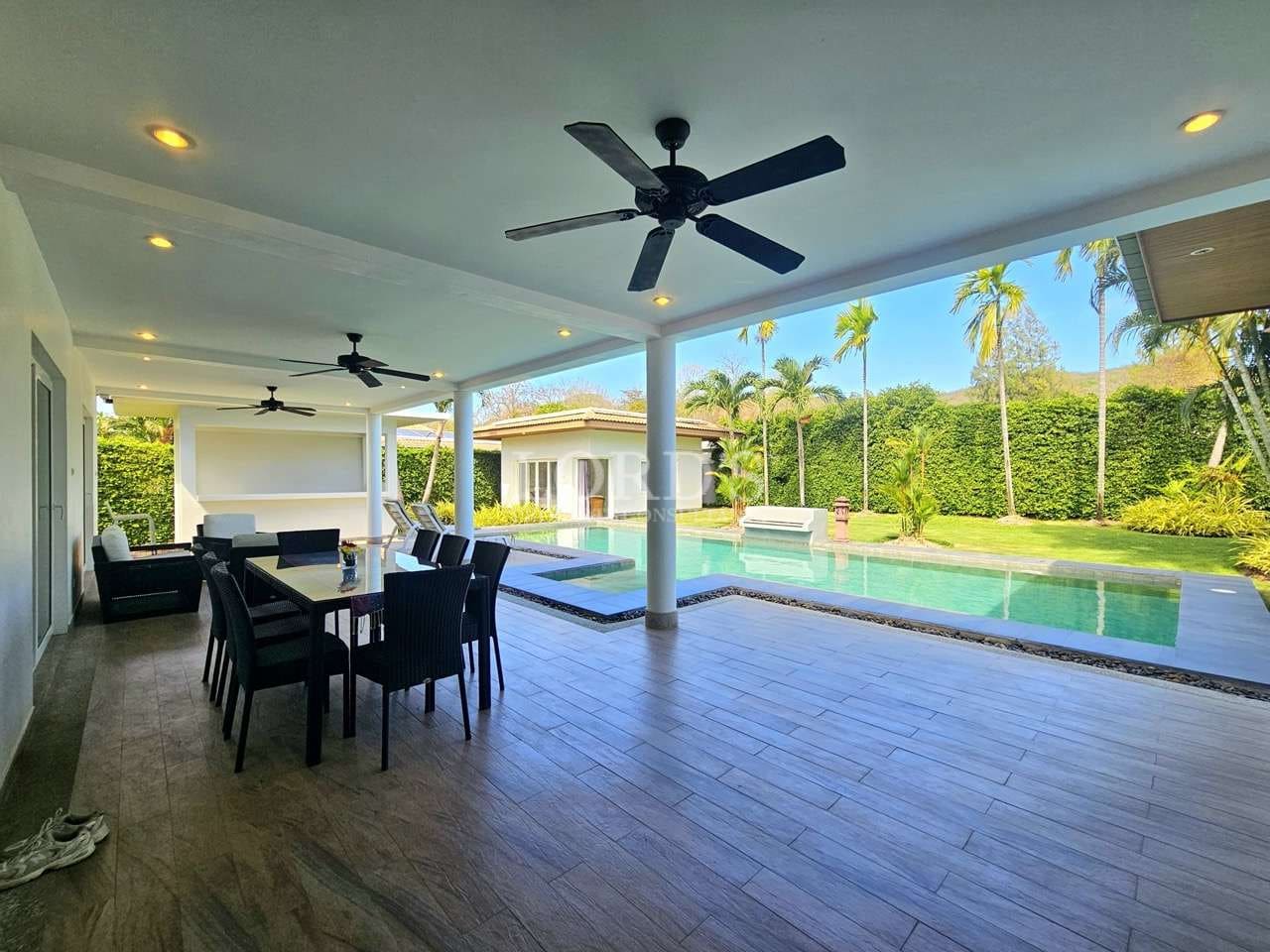 Covered outdoor patio with dining area, ceiling fans, and private swimming pool in a luxury tropical villa.