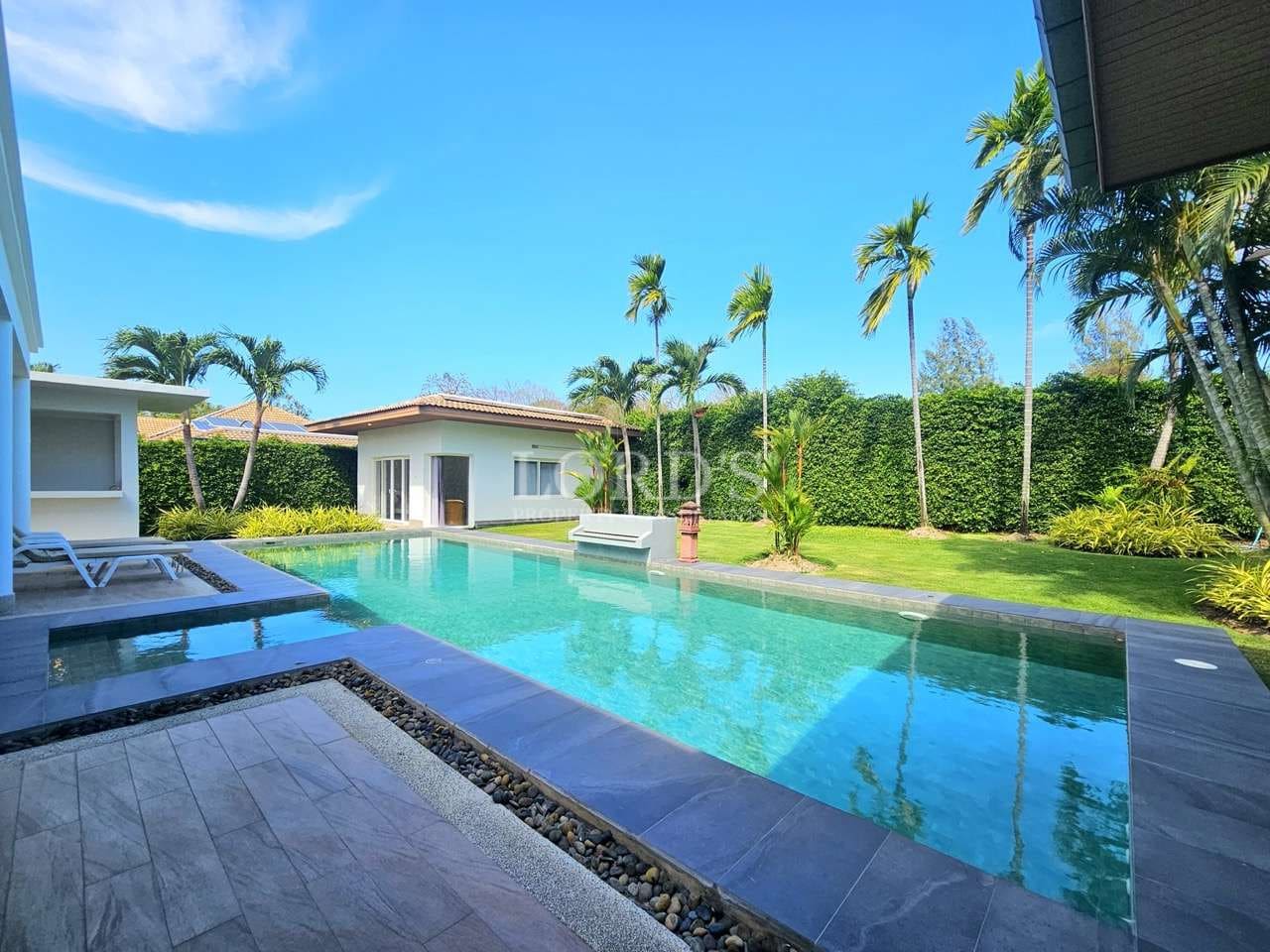 Luxury private villa swimming pool with tropical garden, palm trees, and modern outdoor lounge area.