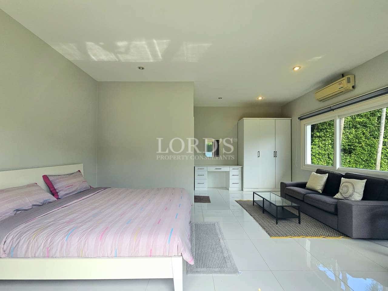 Spacious modern bedroom with king-size bed, sofa seating area, wardrobe, and large window with greenery view.