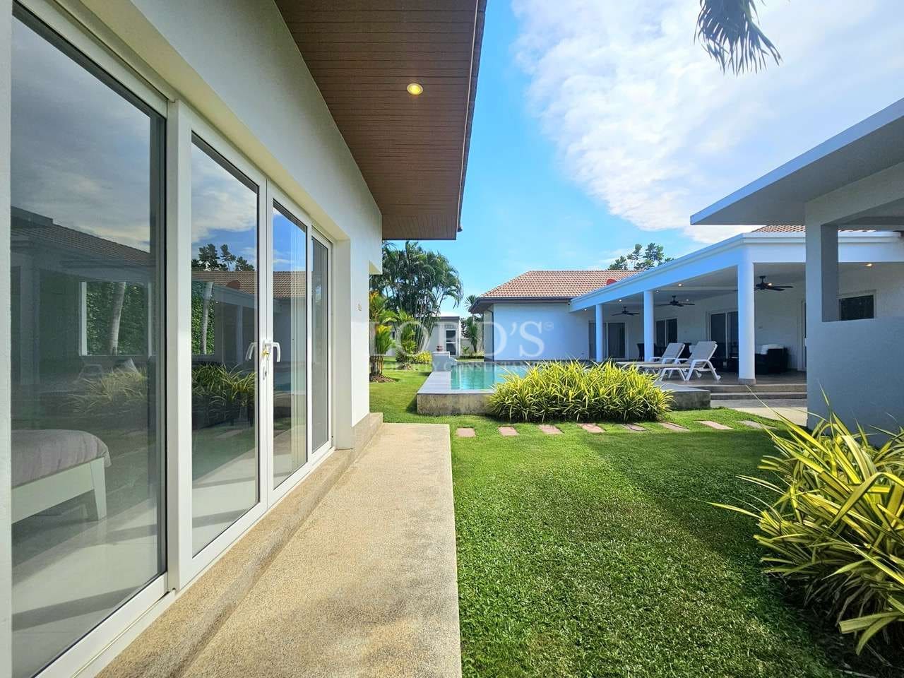 Modern luxury villa exterior with sliding glass doors, landscaped garden, private swimming pool, and outdoor lounge area.