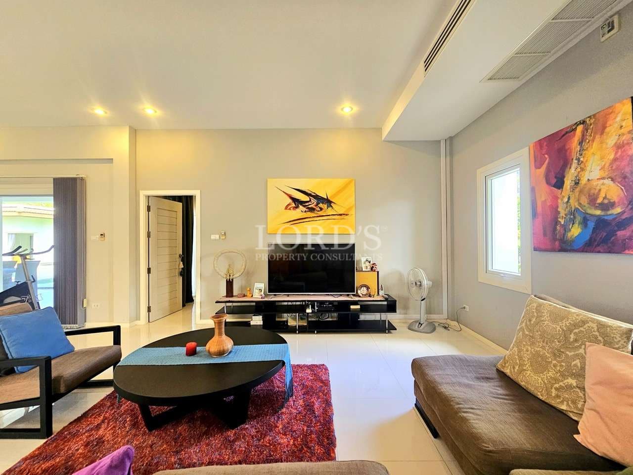 Modern living room with cozy seating, flat-screen TV, abstract wall art, and warm ambient lighting.