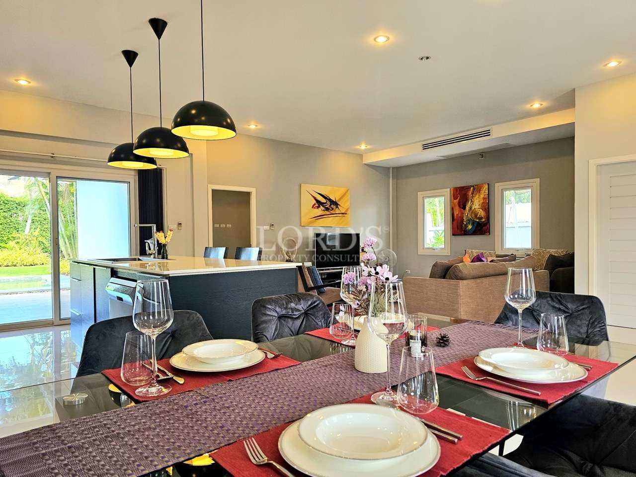 Modern open-plan dining and living area with a kitchen island, pendant lights, set dining table, and contemporary décor.