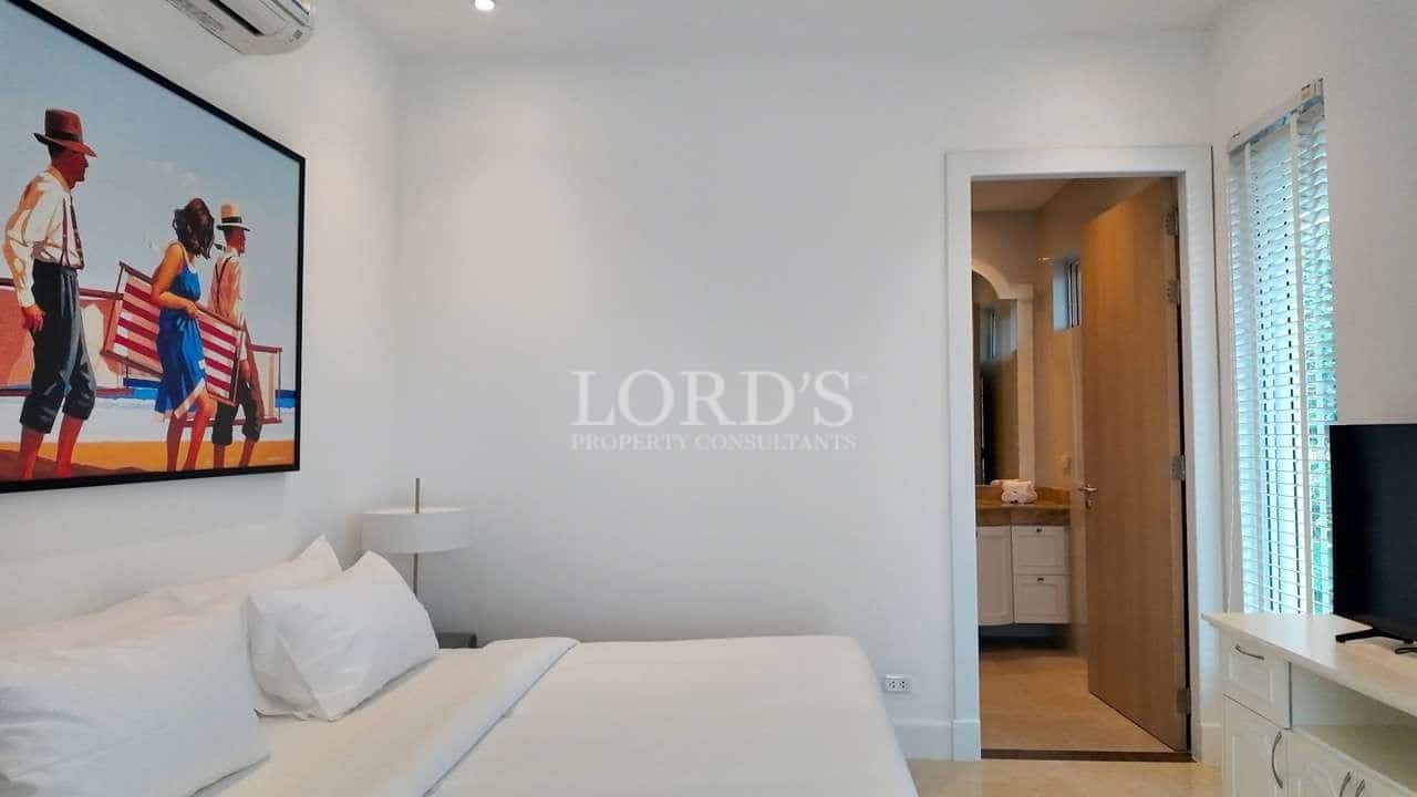 Modern minimalist bedroom with white bedding, wall art, and en-suite bathroom entrance.
