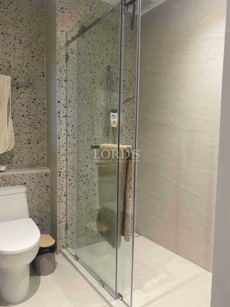 Modern bathroom with glass shower enclosure, terrazzo accent wall, neutral tiles, and minimalist fixtures.