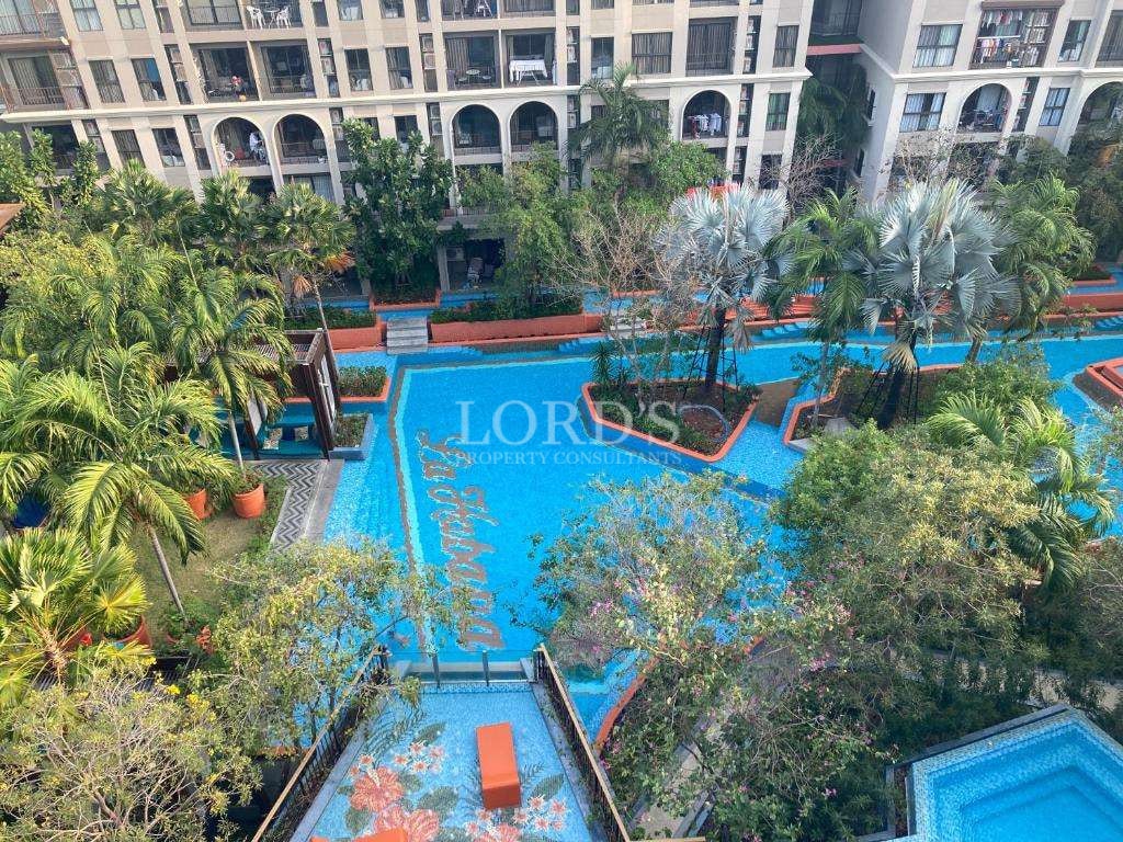 Aerial view of a luxury residential complex with a lagoon-style swimming pool, tropical landscaping, palm trees, and elegant apartment balconies.