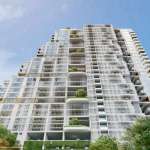 Modern high-rise residential building with stepped architecture, glass balconies, vertical greenery, and a contemporary white facade under a clear blue sky.