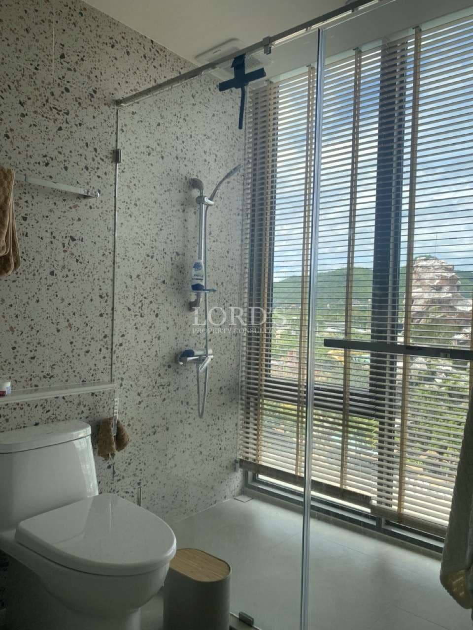 Modern bathroom with glass shower enclosure, terrazzo-style wall tiles, window blinds, and contemporary fixtures.