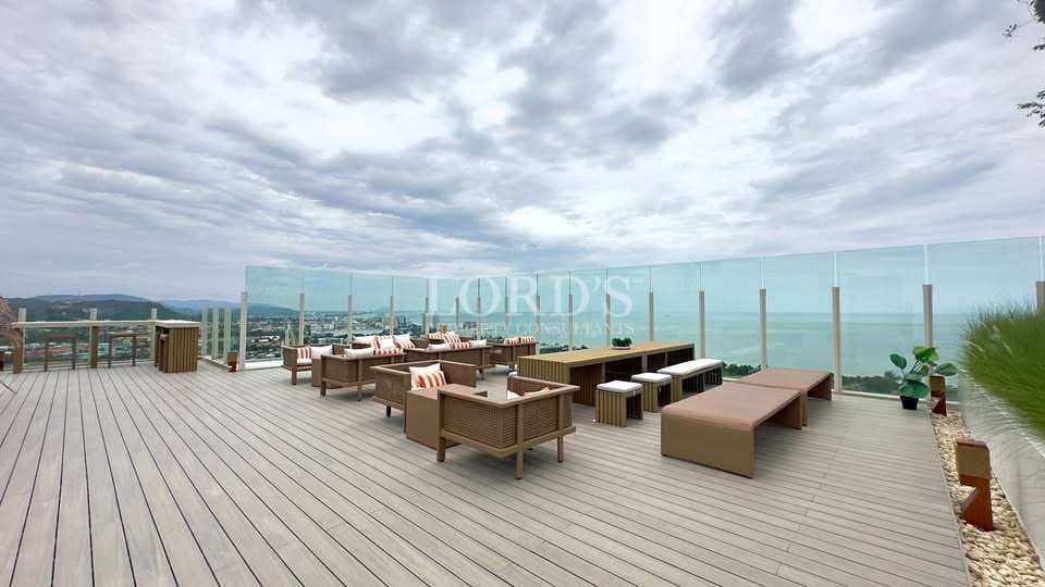 Luxury rooftop terrace with modern outdoor seating, wooden deck flooring, glass railing, and panoramic ocean and city views under a cloudy sky.