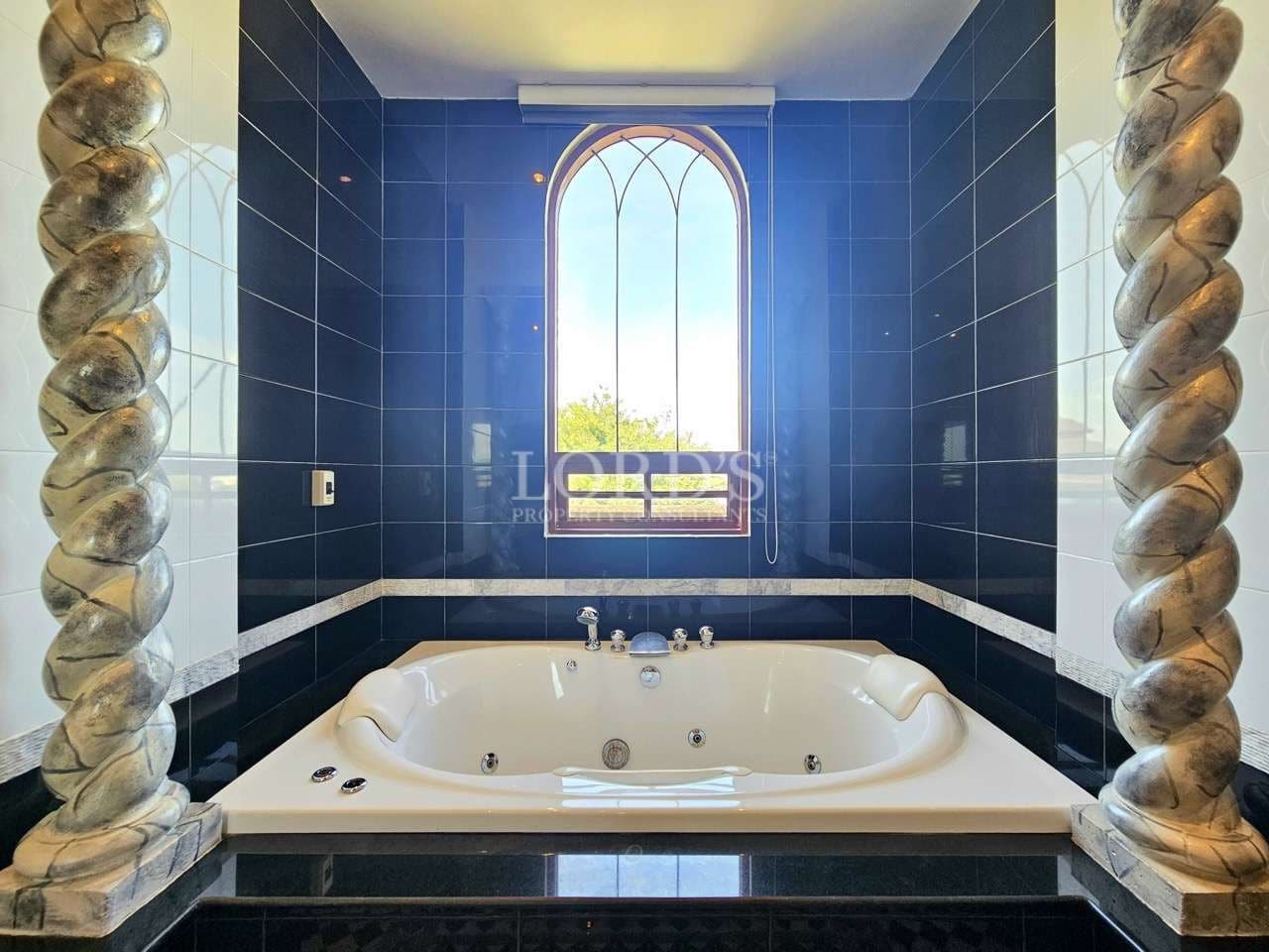 Luxury bathroom with jacuzzi bathtub, dark tiled walls, and arched window design.