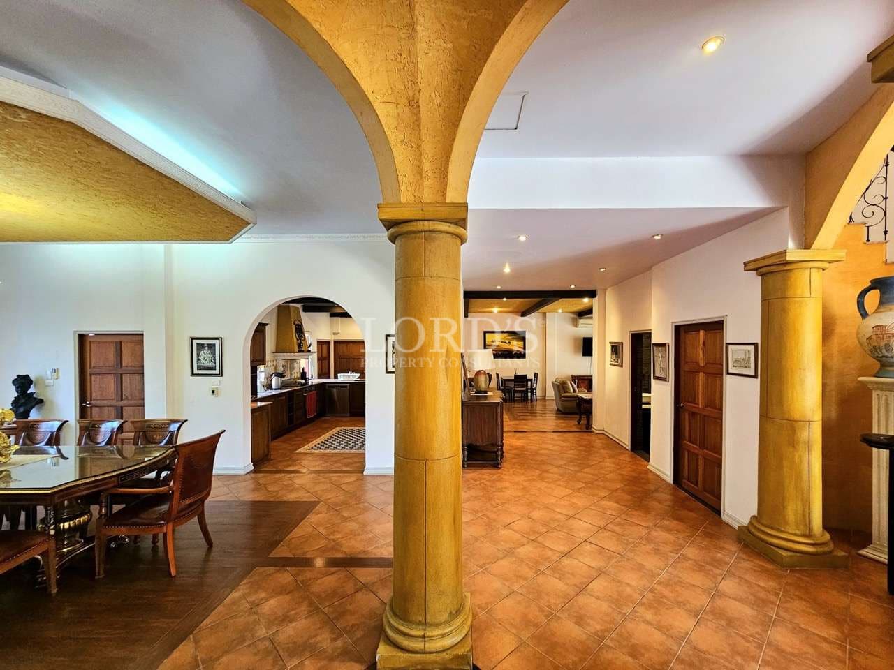 Luxury villa interior with arched columns, open-plan living and dining area, and tiled flooring.