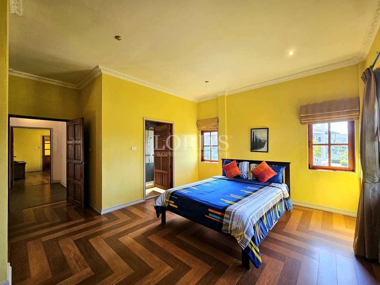 Bright luxury bedroom with yellow walls, wooden flooring, large bed, and natural light from windows.