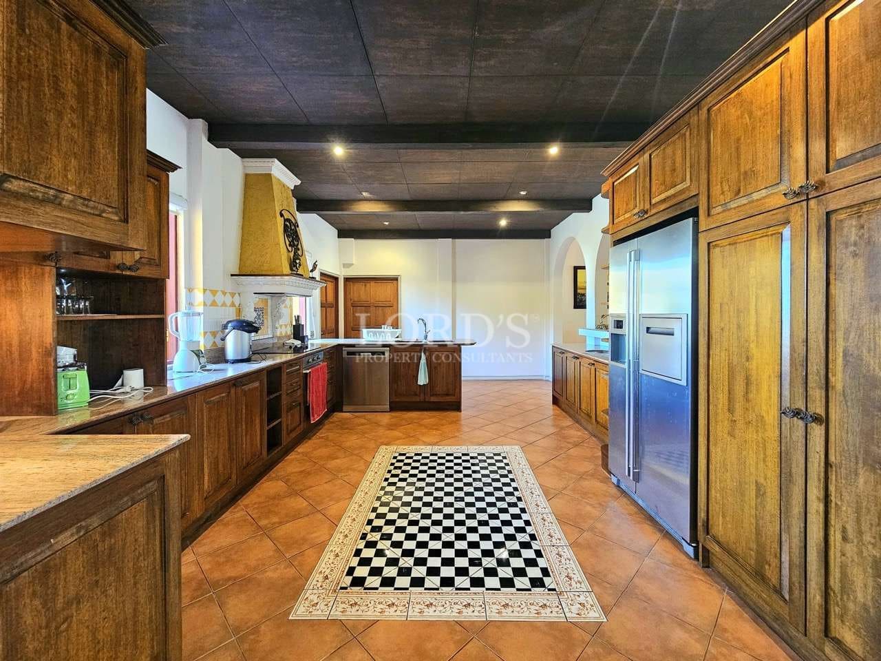 Spacious luxury kitchen with solid wood cabinetry, stainless steel refrigerator, island counter, and tiled flooring.