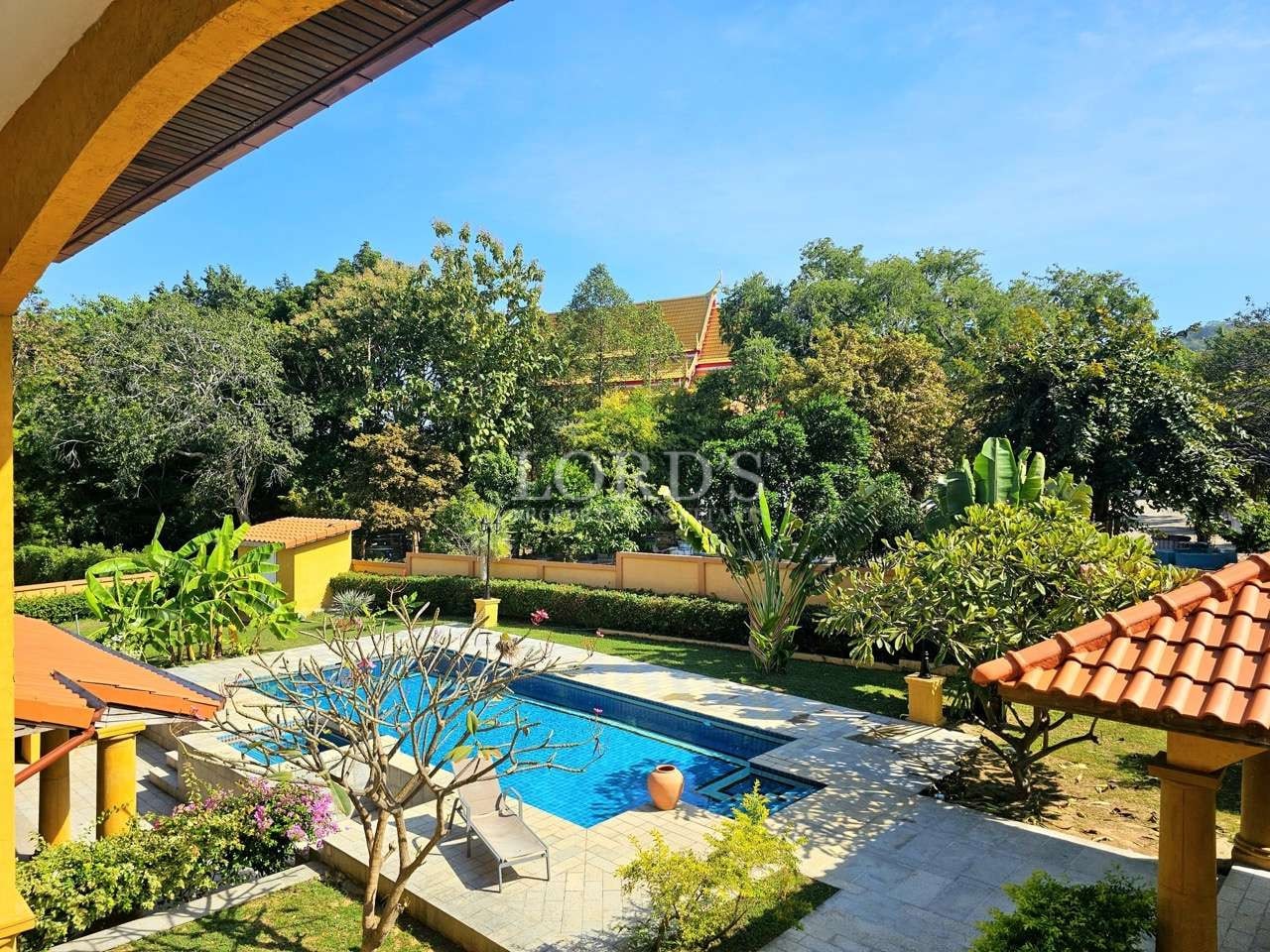 Private swimming pool surrounded by landscaped garden and tropical greenery, viewed from a villa balcony.
