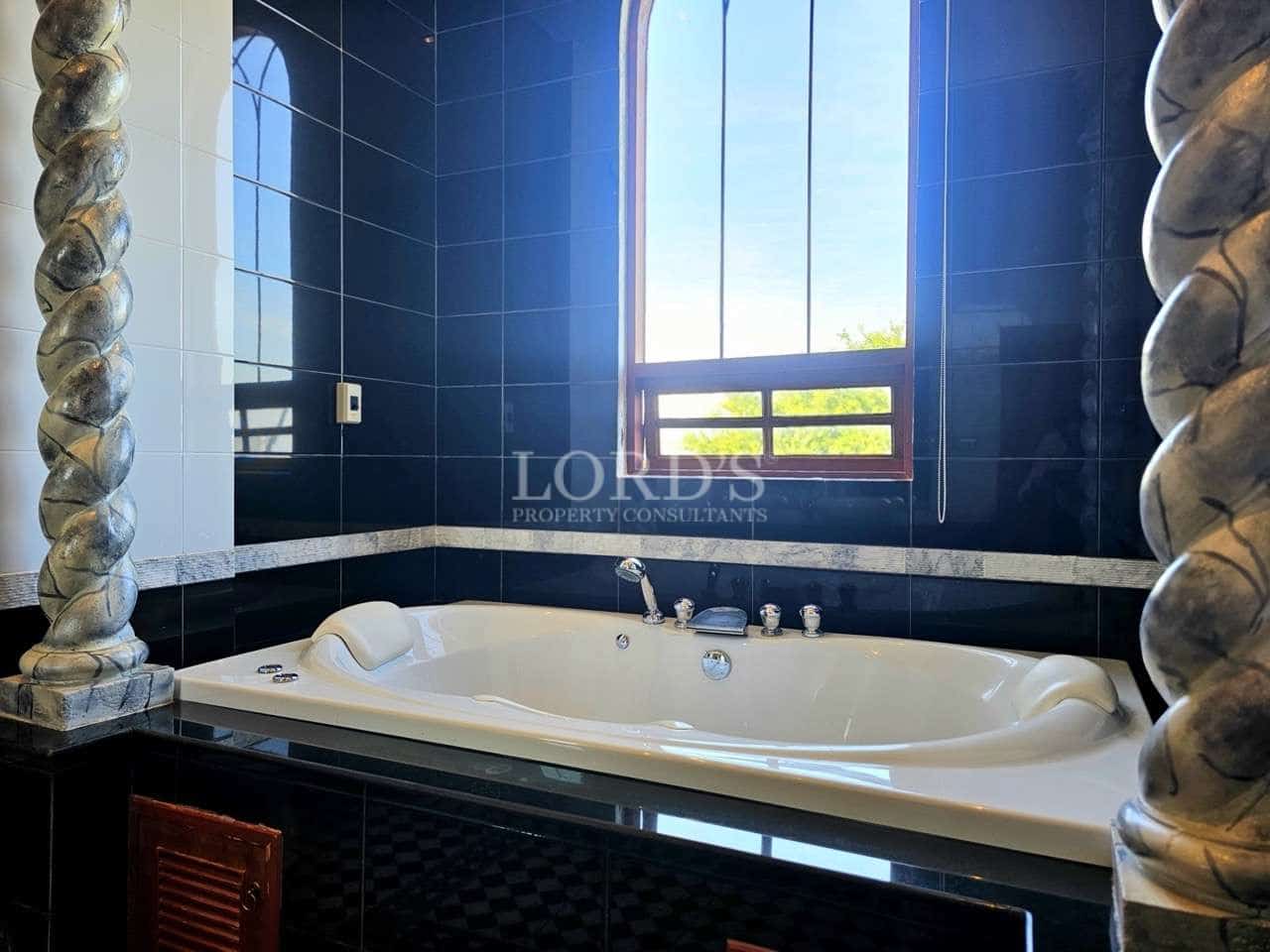 Luxury bathroom with built-in jacuzzi bathtub, black tiled walls, and large arched window.