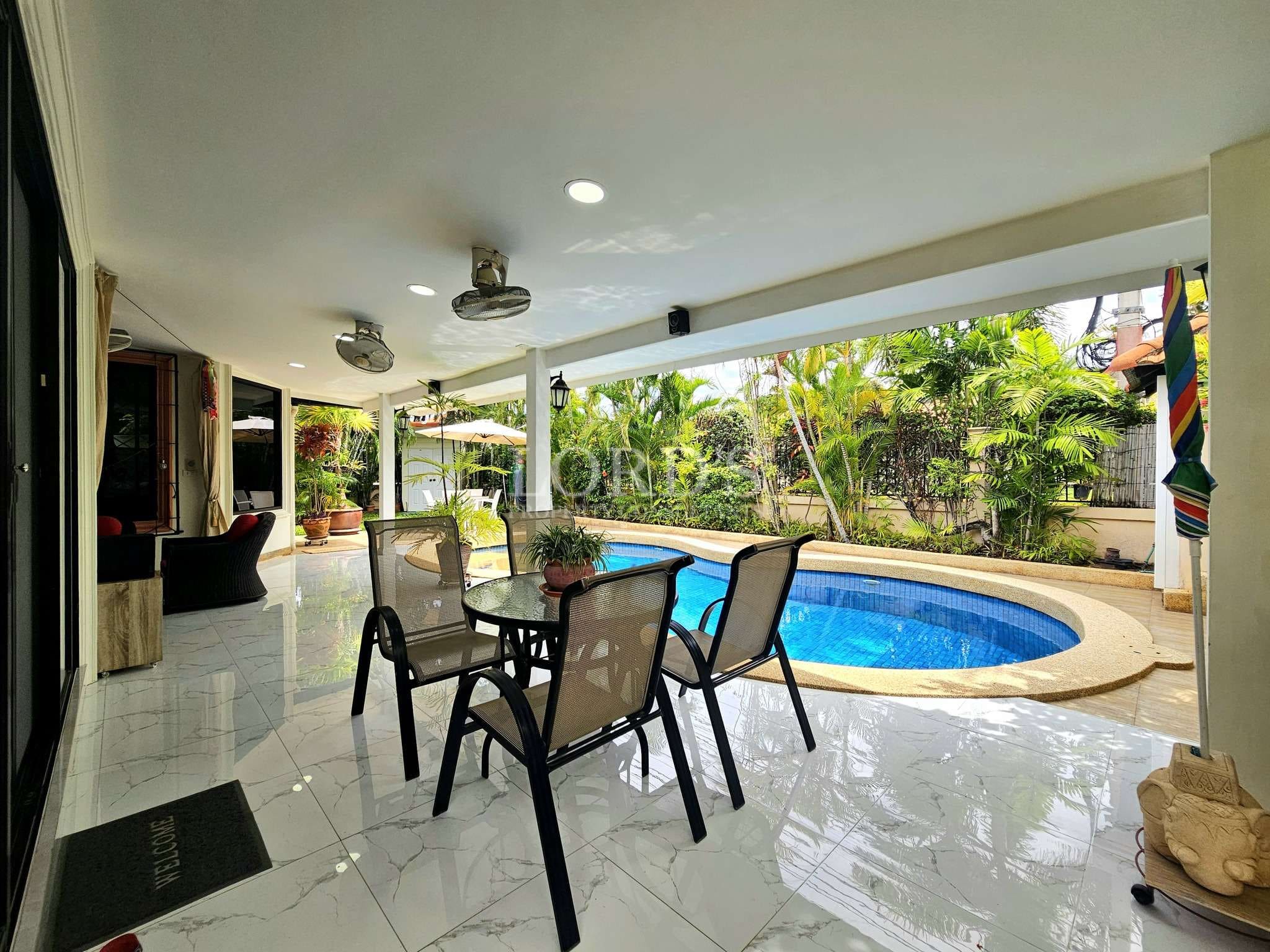 Covered outdoor patio with dining set, ceiling fans, and private swimming pool surrounded by tropical greenery