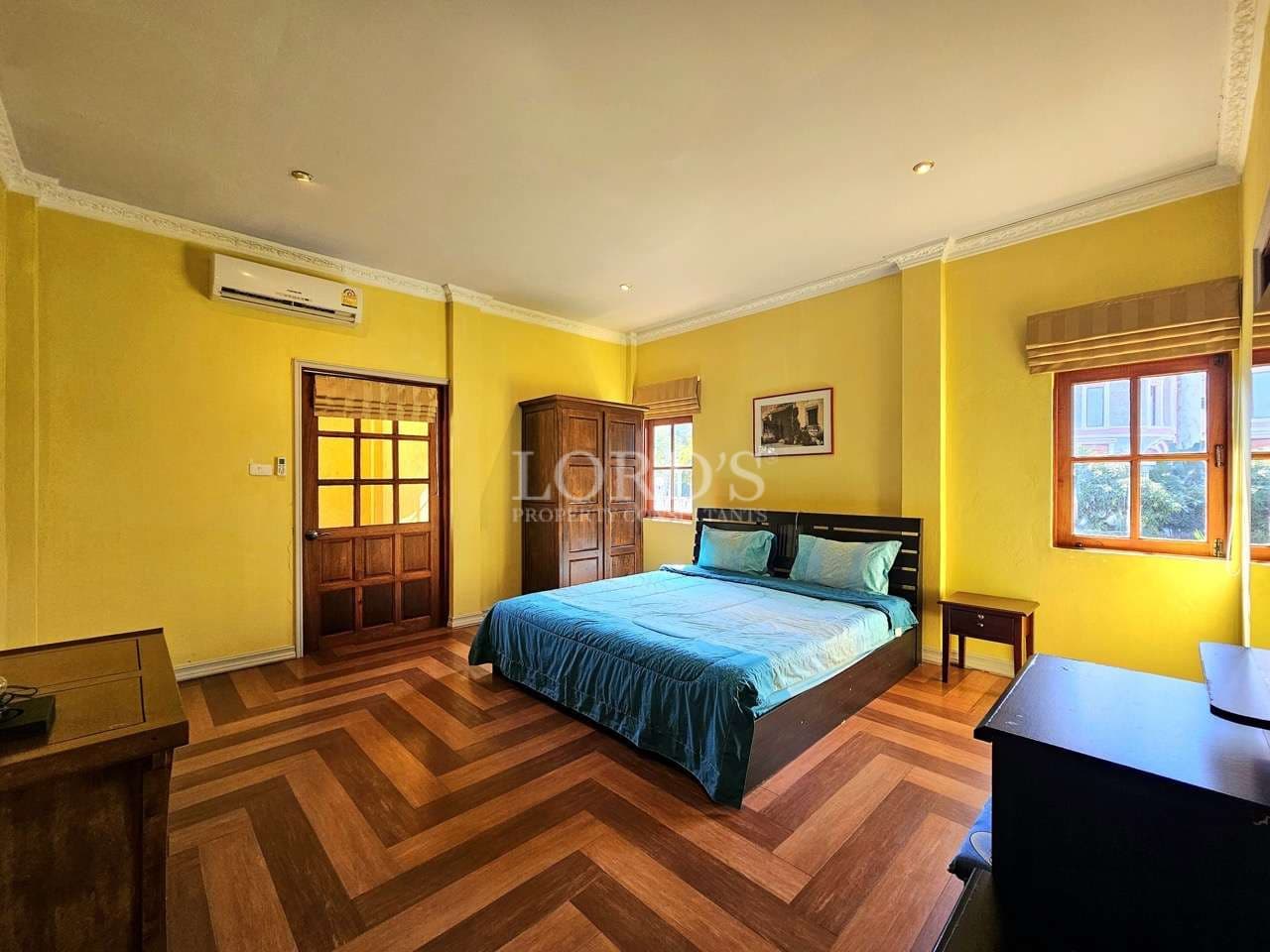 Spacious bedroom with wooden flooring, yellow walls, and a double bed in a luxury villa.