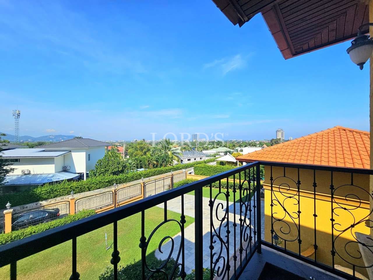Luxury villa balcony with wrought iron railing overlooking landscaped garden, neighboring homes, and clear blue sky.