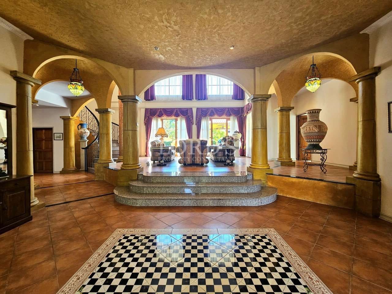 Grand luxury villa interior with arched columns, elevated living area, classic furniture, and elegant Mediterranean-inspired design.