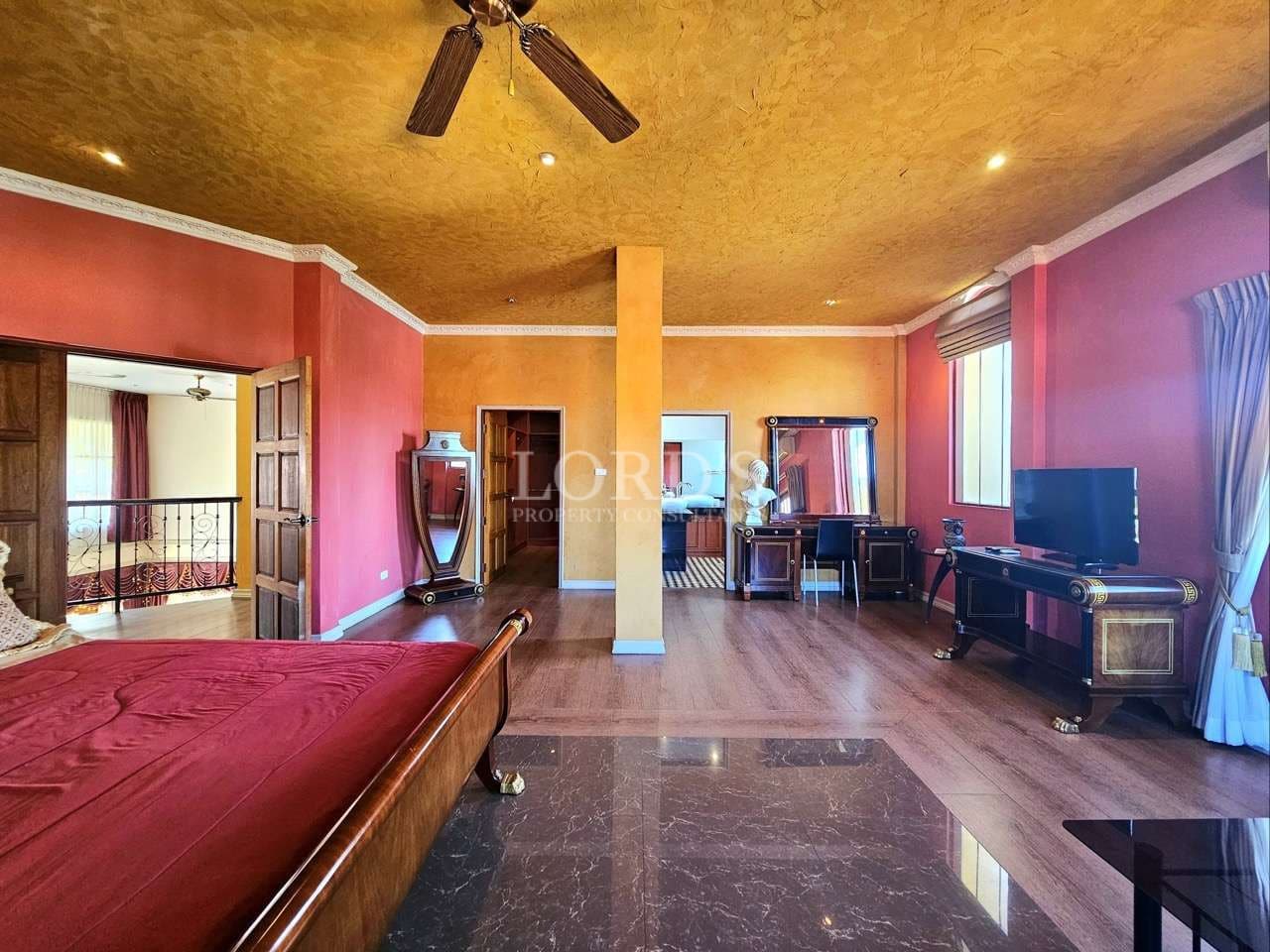 Spacious luxury bedroom with warm textured ceiling, wooden flooring, classic furniture, and elegant decor in a high-end villa interior.