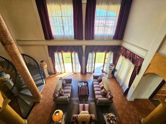 Luxury double-height living room with classic interior design, tall windows, elegant draped curtains, symmetrical sofa seating, and natural light-filled space.