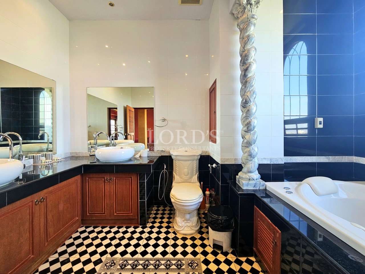 Luxury classic bathroom with freestanding bathtub, ornate twisted column detail, double vanity sinks, black and white patterned tile flooring, and high-gloss wall tiles.