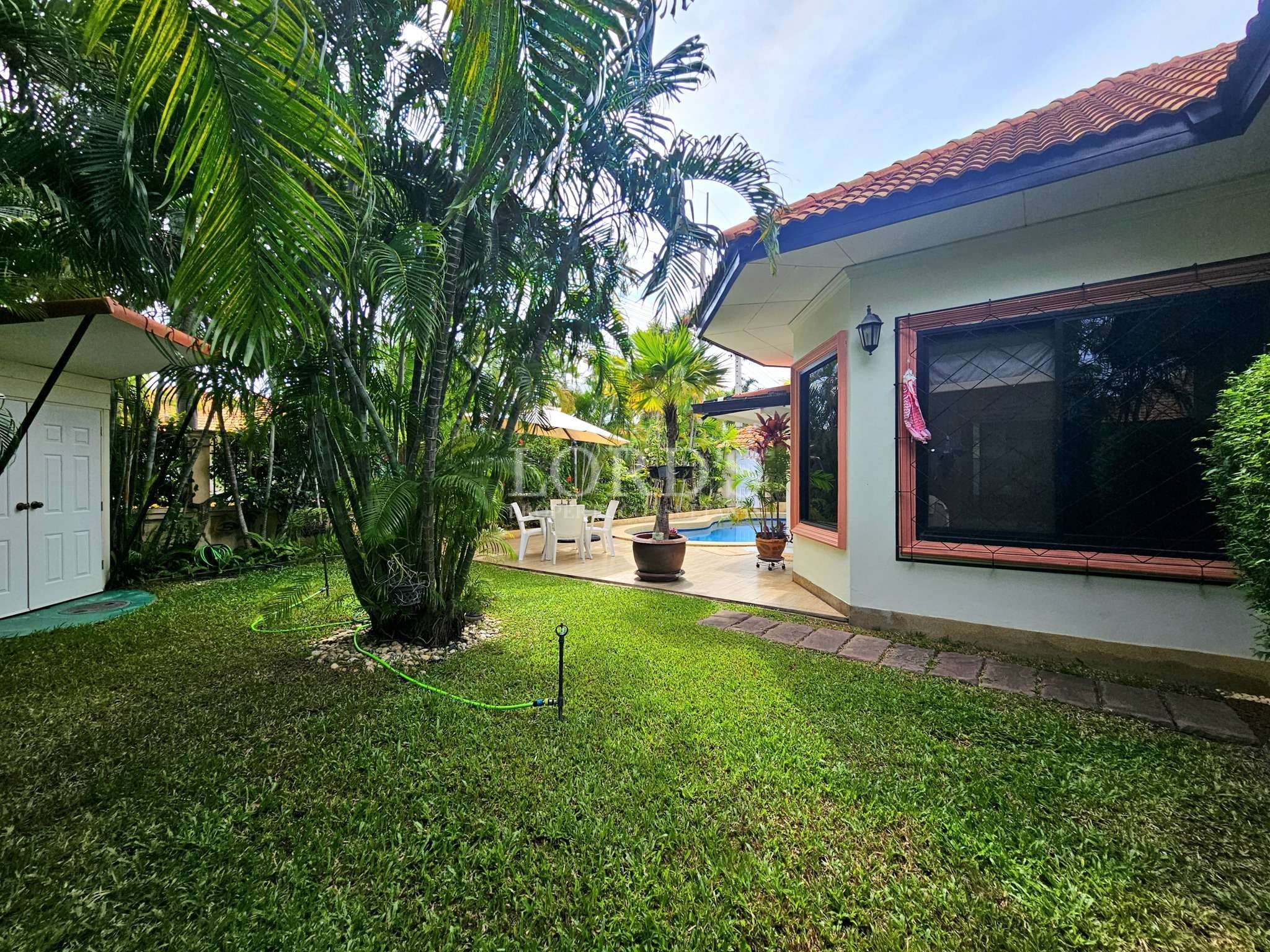 Lush tropical garden courtyard with palm trees, green lawn, and patio seating beside a villa.