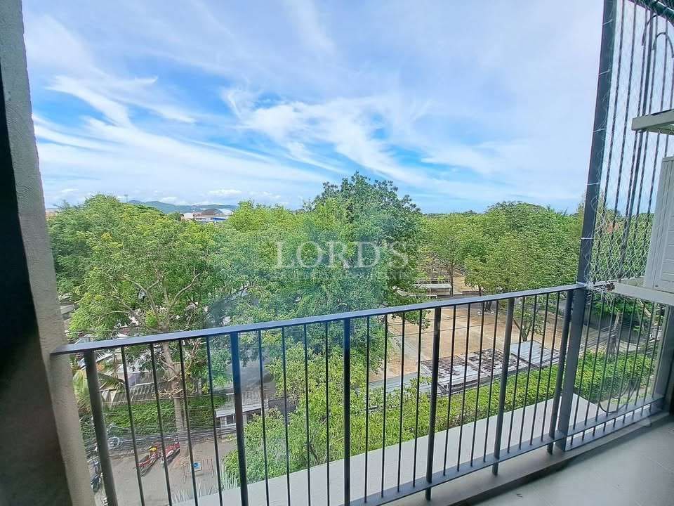 Balcony view from modern apartment overlooking lush green trees, open sky, and a quiet neighborhood street.