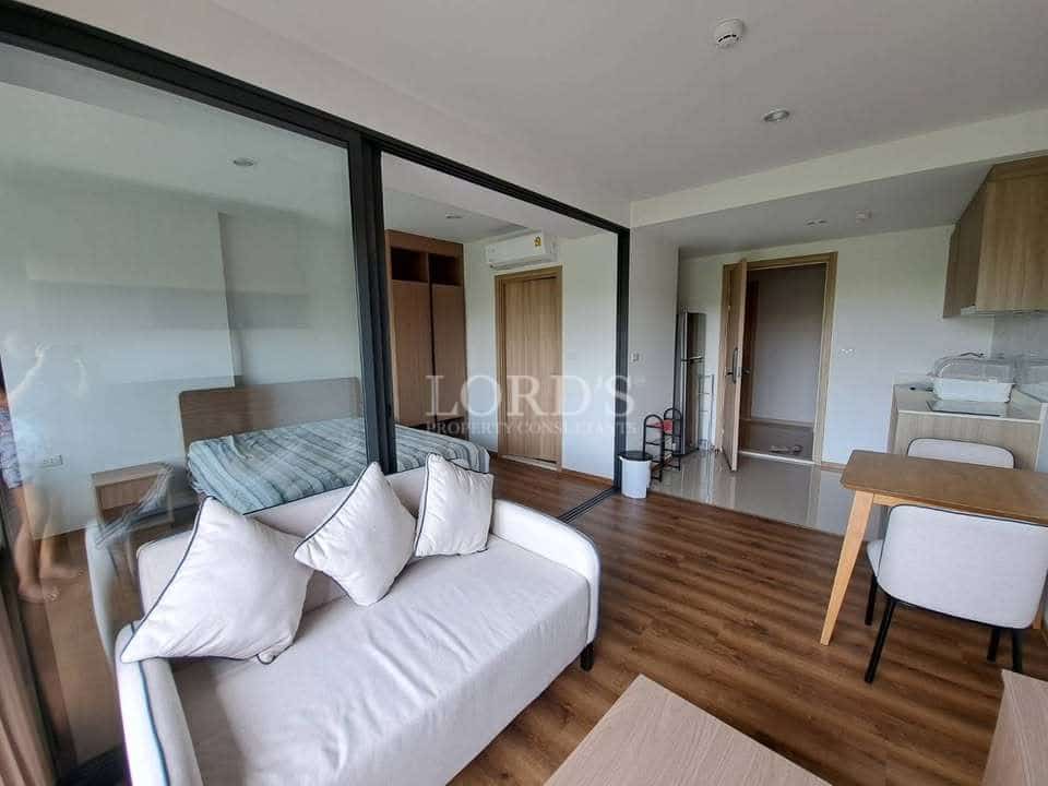 Modern one-bedroom condo interior with glass partition, sofa seating area, wooden flooring, and compact dining space.