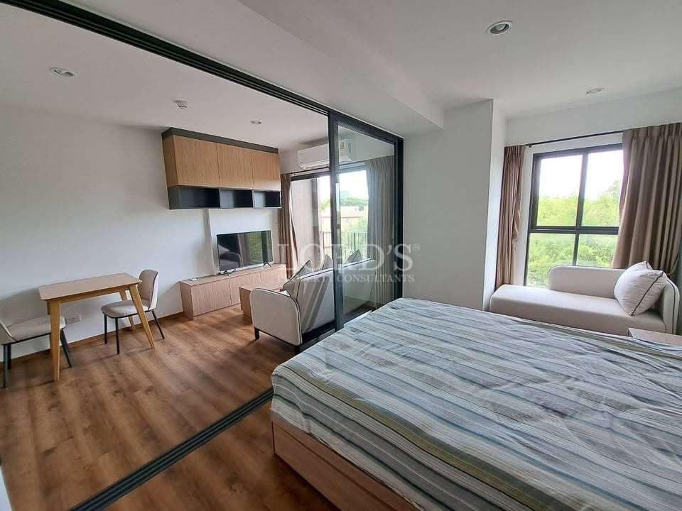 Modern studio condominium bedroom with glass partition, wooden flooring, compact workspace, and natural light from large window.