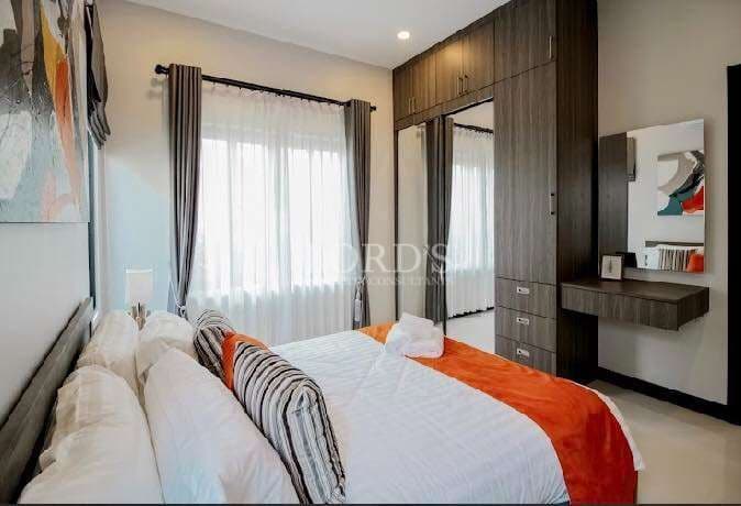 Modern bedroom with built-in wardrobe, work desk, soft curtains, and orange accent bedding.