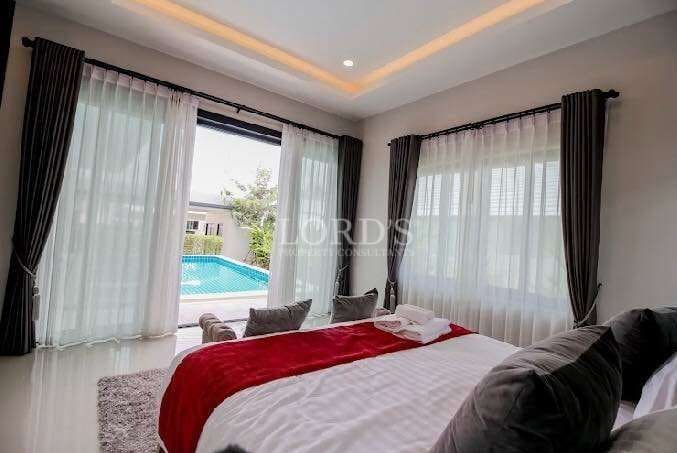 Modern bedroom with large glass windows, sheer curtains, and pool view in a luxury villa.