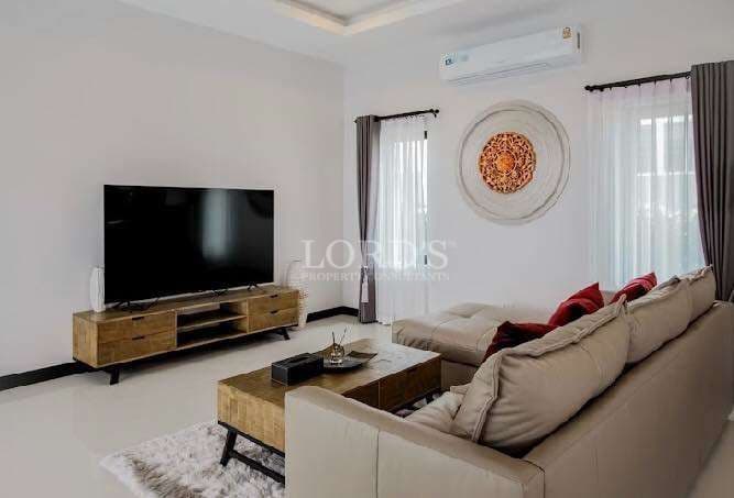Modern living room with sectional sofa, wall-mounted TV, wooden furniture, and soft natural light.