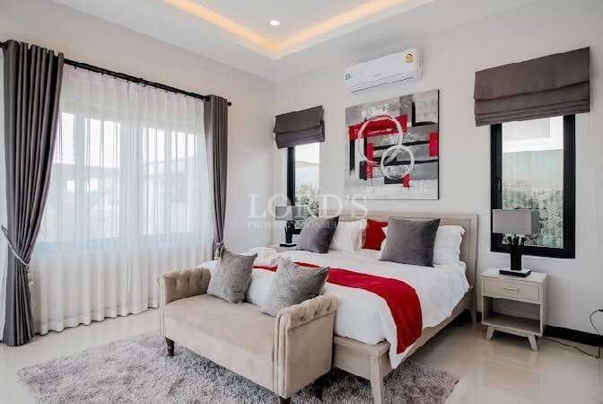 Modern luxury bedroom with upholstered bed, red accent bedding, bench seating, and large windows.