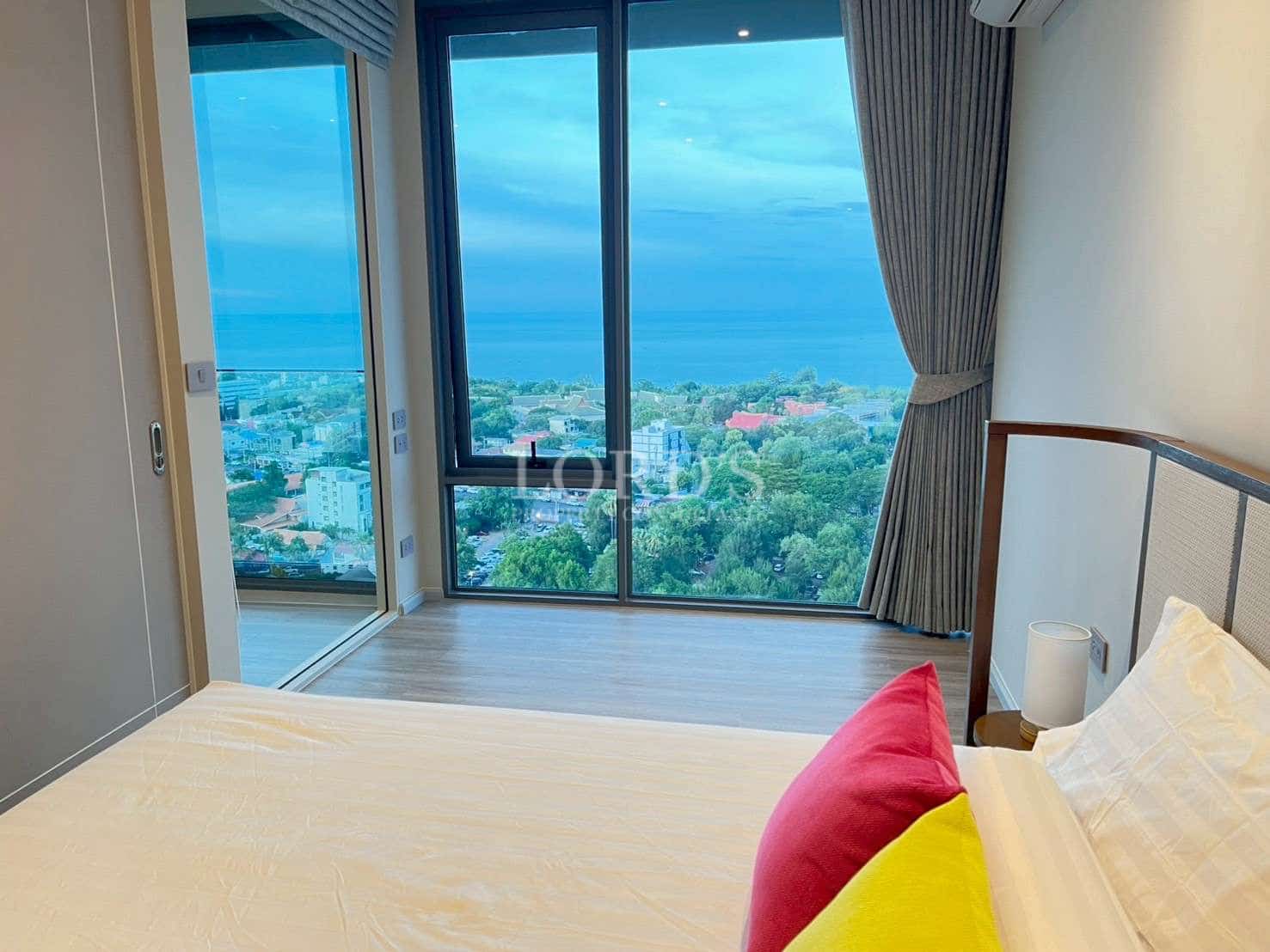 Modern bedroom with floor-to-ceiling windows offering panoramic sea and city views.
