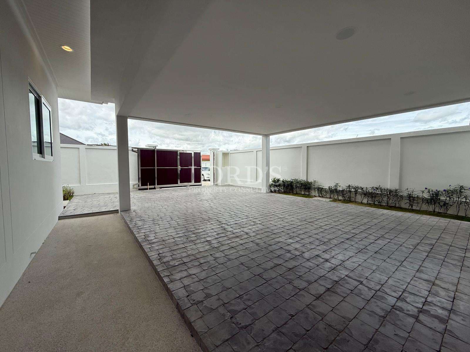 Covered private driveway and parking area of a modern luxury villa with paved flooring.