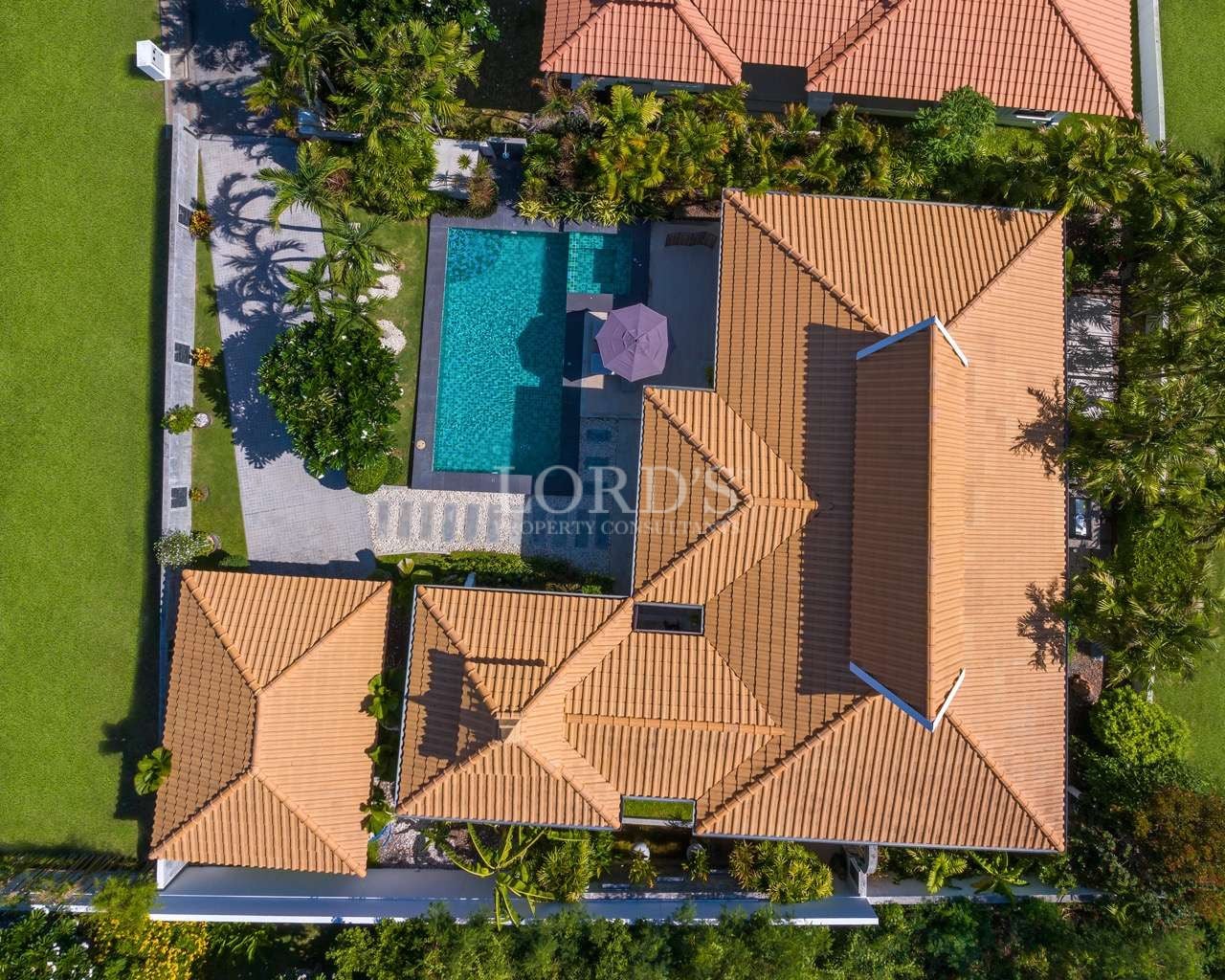 Aerial view of a luxury villa with private swimming pool, tiled roof, and landscaped tropical garden.