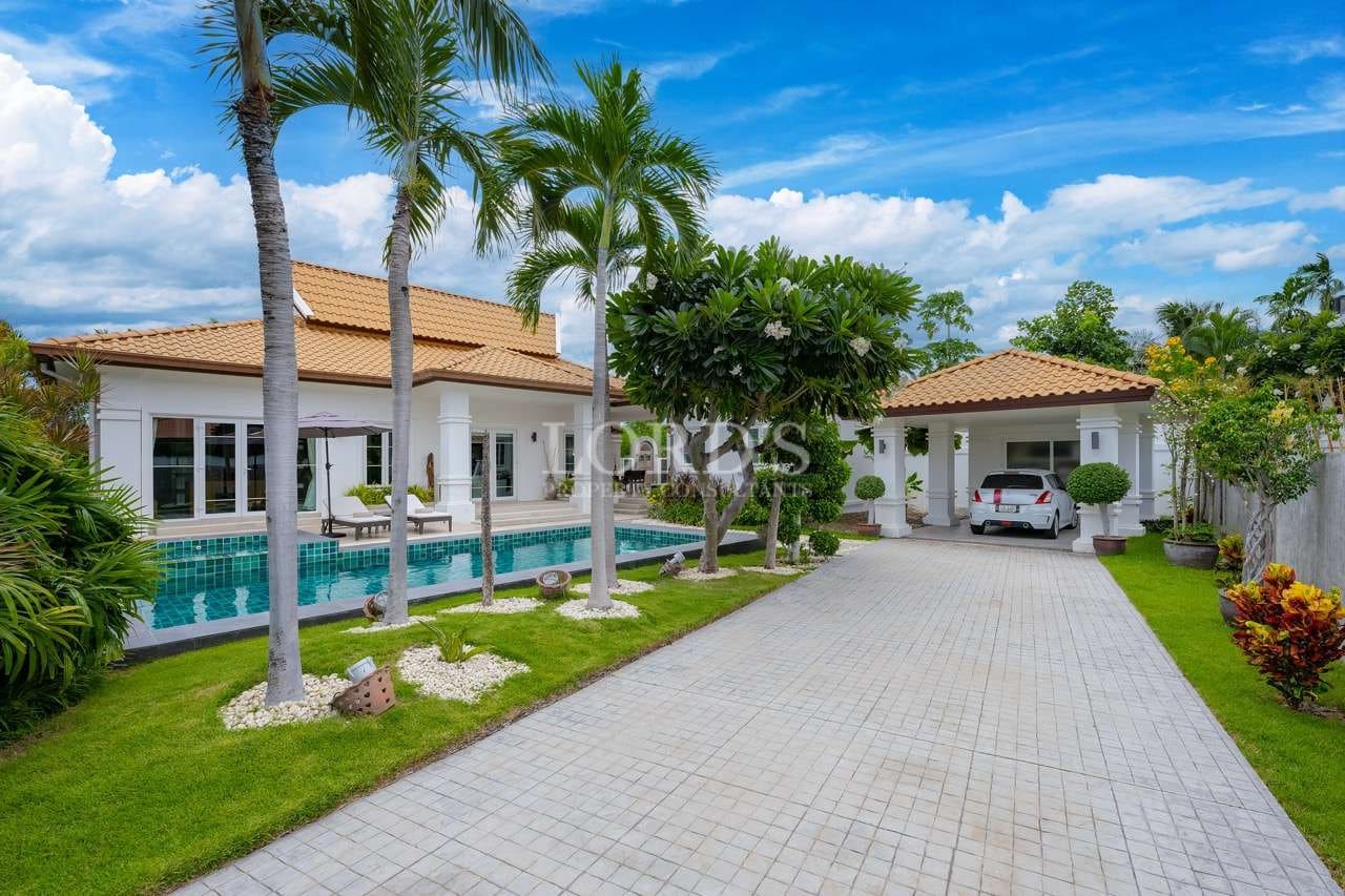 Luxury tropical villa with palm-lined driveway, private swimming pool, covered carport, and landscaped garden.