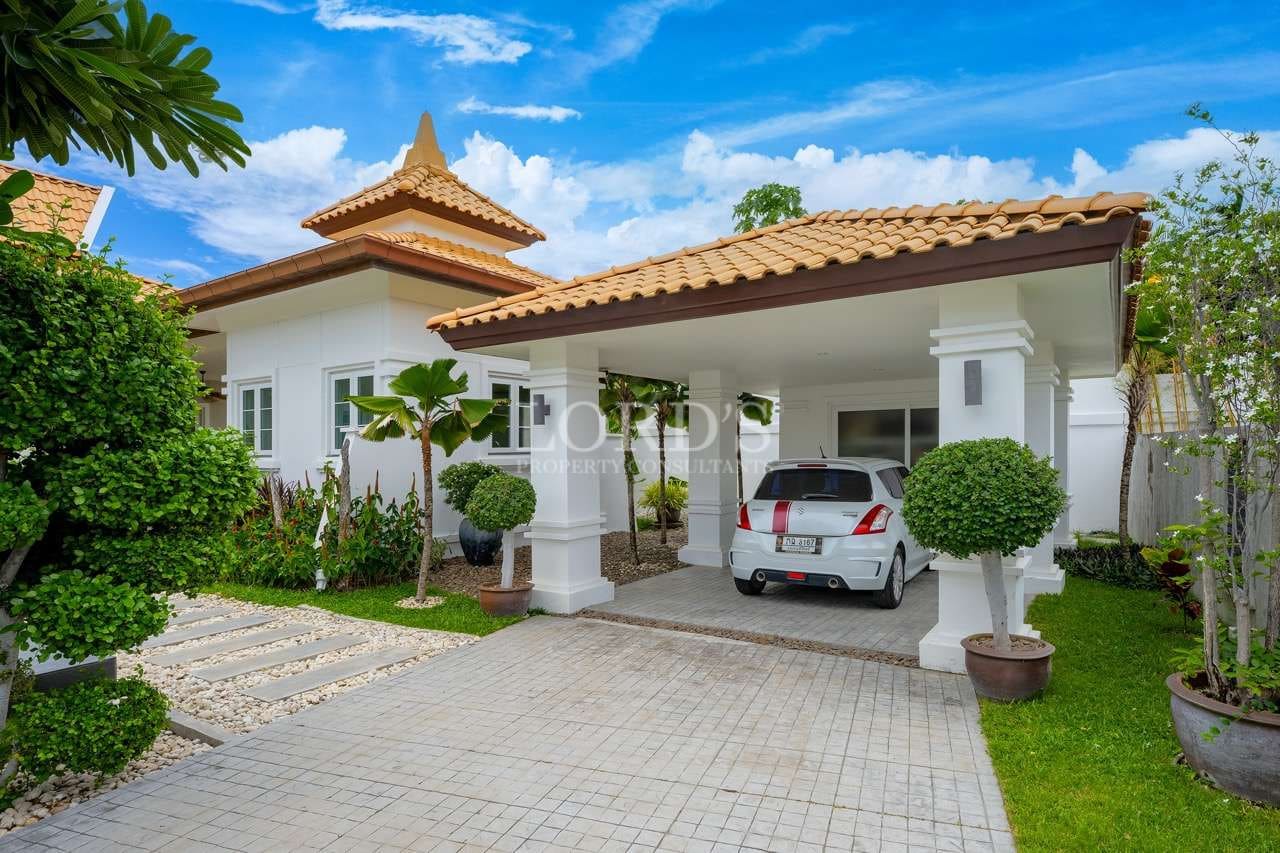 Luxury white villa with covered carport, tiled roof, landscaped garden, and private driveway.