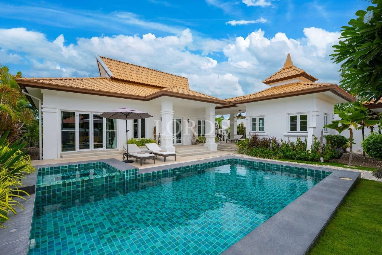 IMG-1018 Groß Luxury modern villa with private swimming pool, sun loungers, and landscaped tropical garden under blue sky.